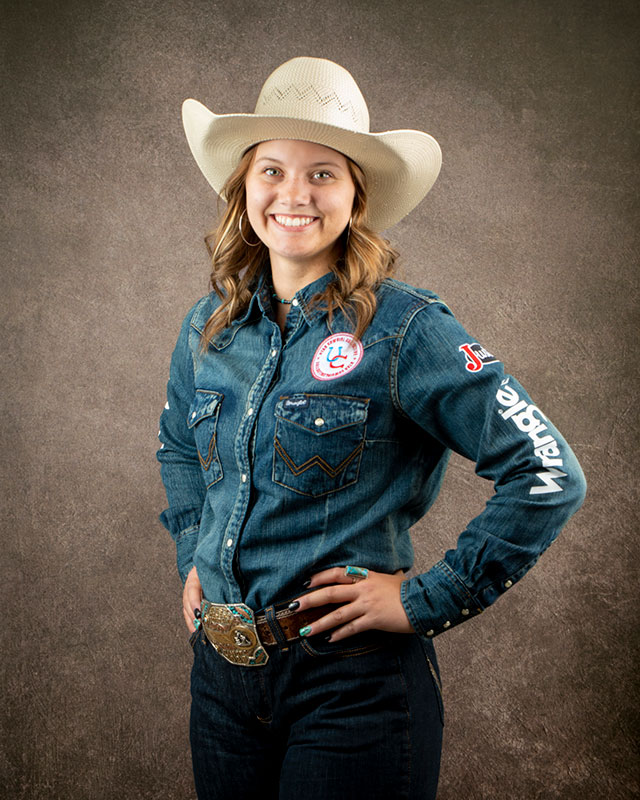 McKenna Addington smiling at the camera, posing wearing a denim shirt and cowgirl hat.